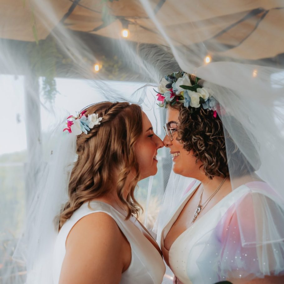 A wooden table with two chairs flanked by floral arrangements against a stone wall.